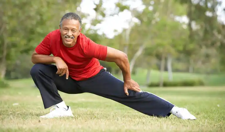 Older adult man stretching outdoors in a park, demonstrating flexibility and bone-strengthening exercise.