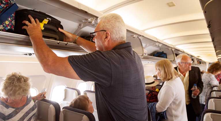 Senior lifting his hand lugagge to put it in the overhead compartment