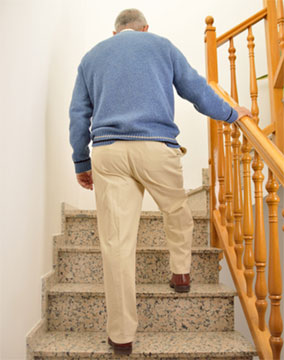 Senior climbing stairs while holding the handrail