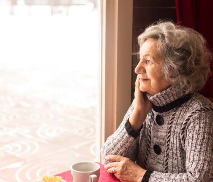 Senior woman having coffee and staying by the window during the pandemic